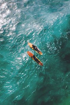 two people on surfboards in the middle of an ocean with green water and blue sky