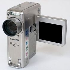 a silver digital camera sitting on top of a white table next to a small screen