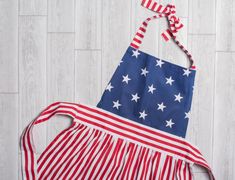 an american flag apron hanging on a white wooden wall with red, white and blue stripes