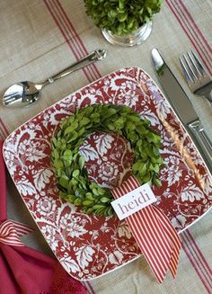 a red and white plate with a green wreath on it next to utensils