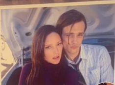 a man and woman sitting next to each other in front of a painting on the wall