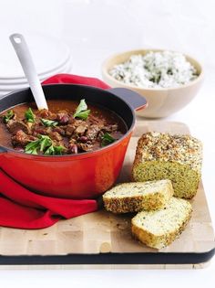 a red pot filled with meat and bread on top of a cutting board next to other foods