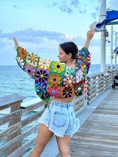 a woman standing on a pier with her arms in the air while wearing a colorful sweater