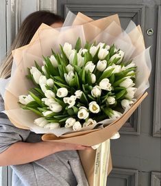 a woman holding a bouquet of white tulips in front of a gray door