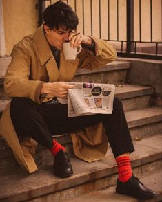 a man is sitting on the steps drinking coffee and reading a newspaper with red socks