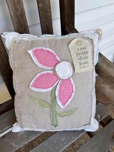 a pillow with a pink flower on it sitting on a wooden chair next to a wall