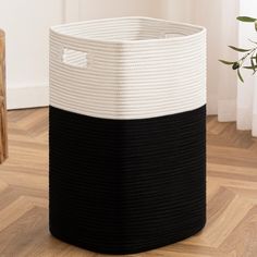 a black and white basket sitting on top of a wooden floor next to a potted plant