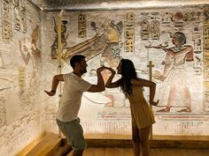 a man and woman standing next to each other in front of an egyptian wall painting