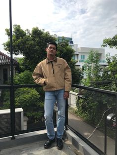 a man standing on top of a balcony next to a fence and trees in the background