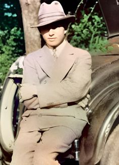 an old photo of a man in a suit and hat sitting next to a car