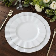 a table setting with white plates, silverware and flowers on the wooden table top