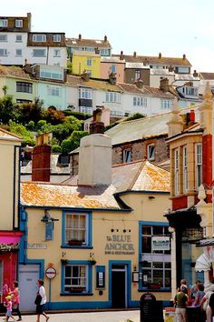 people are walking on the sidewalk in front of some buildings and houses with hills in the background