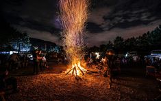 people are gathered around a campfire at night with fireworks in the sky above them