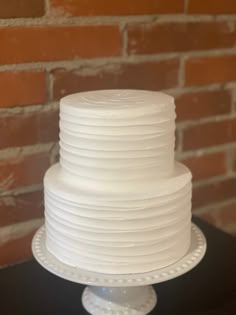 a white frosted cake sitting on top of a table next to a brick wall