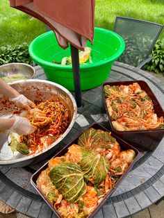 a table topped with pans filled with food next to a green bowl and umbrella