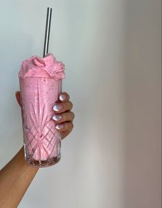 a hand holding a pink drink with a straw in it's mouth and a spoon sticking out of the cup