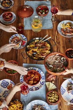 a group of people sitting around a wooden table eating food from bowls and pans