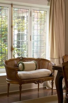 a wicker chair sitting in front of a window next to a table with a pillow on it