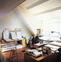 a man sitting at a desk with lots of papers on it in an attic office