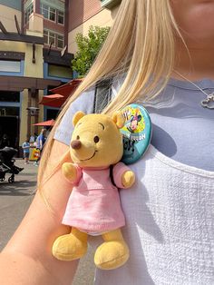 a woman is holding a stuffed bear in her arms and wearing a pink shirt with a button on it's chest