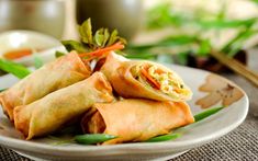 three vegetable spring rolls on a plate with chopsticks next to it and another dish in the background