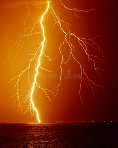 a lightning strike over the ocean at night with bright orange and yellow colors royalty images