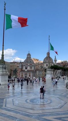 many people are walking around with flags flying in the air and buildings in the background