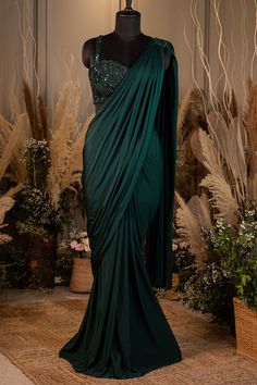 a green dress on display in front of some plants and flowers, with the top draped over it's shoulder