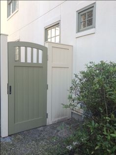 a white house with a green gate and bushes in front of the door is shown