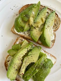 two pieces of bread topped with avocado and other toppings on a white plate