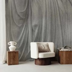 a white chair sitting on top of a wooden table next to a wall covered in curtains