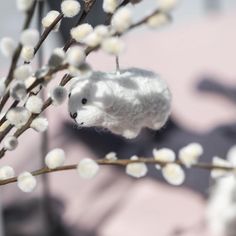 a white stuffed animal hanging from a twig on top of a branch with flowers