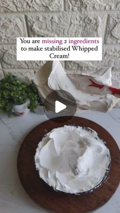 a cake with white frosting on top sitting on a wooden platter next to a brick wall