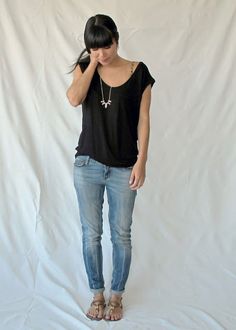 a woman standing in front of a white backdrop wearing blue jeans and a black top