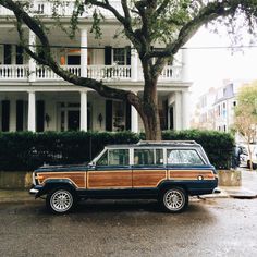 an old station wagon parked in front of a large white house