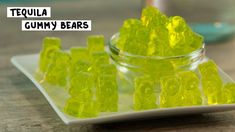 small yellow gummy bears sitting on a white plate next to a glass jar with the word tequila gummy bears in it