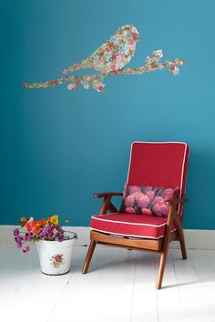 a red chair sitting in front of a blue wall next to a potted plant