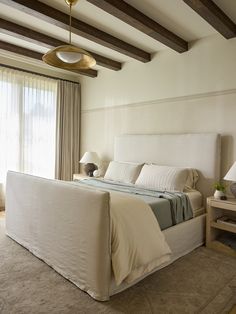 a large bed in a bedroom next to a window with drapes on the windowsill