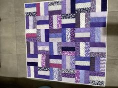 a purple and white patchwork quilt hanging on the wall next to a blue chair