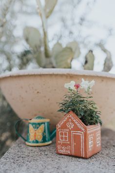 a small house planter sitting on top of a stone wall next to a potted plant