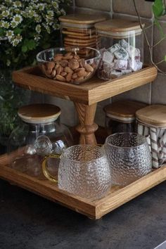 three tiered serving tray with glass jars and nuts on it, sitting next to a potted plant