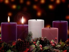 three lit candles surrounded by holly and pine cones