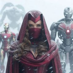 a woman in a red cape standing next to two iron man figures on a snowy day