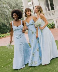 three beautiful women standing next to each other on a grass covered field in front of a house