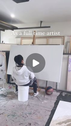 a woman sitting on top of a bucket next to an easel