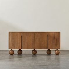 a wooden cabinet sitting on top of a cement floor next to a white wall and two brown vases