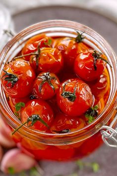 a glass jar filled with cherry tomatoes on top of a wooden table next to a hand holding