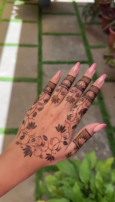 a woman's hand with henna tattoos on it and green plants in the background