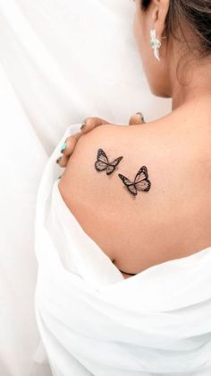 a woman's back with two butterflies on her left shoulder and the upper part of her right arm