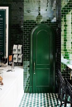 a green door in a black and white tiled room with tables, chairs and stools